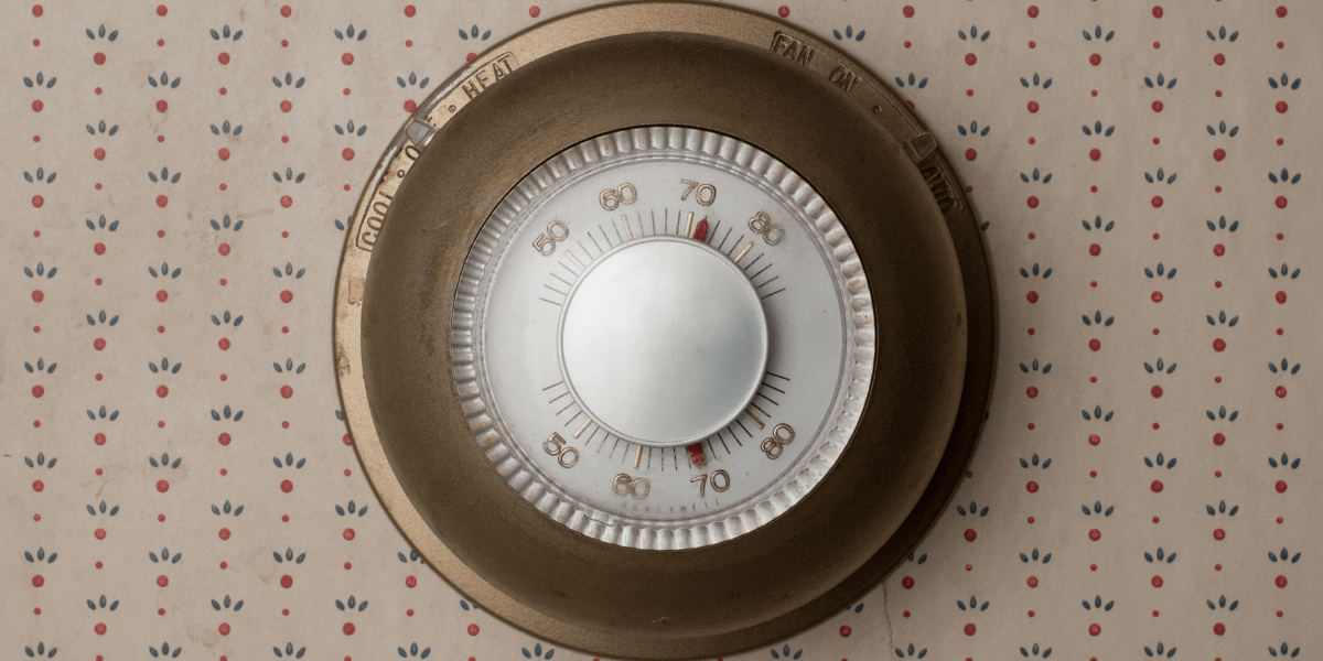 A vintage thermostat dial on wall with wallpaper