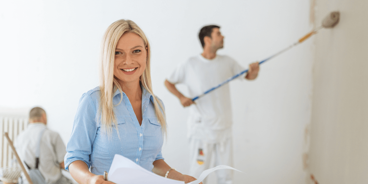 Woman holding papers while man is painting walls with a roller brush | Arizona Property Manager